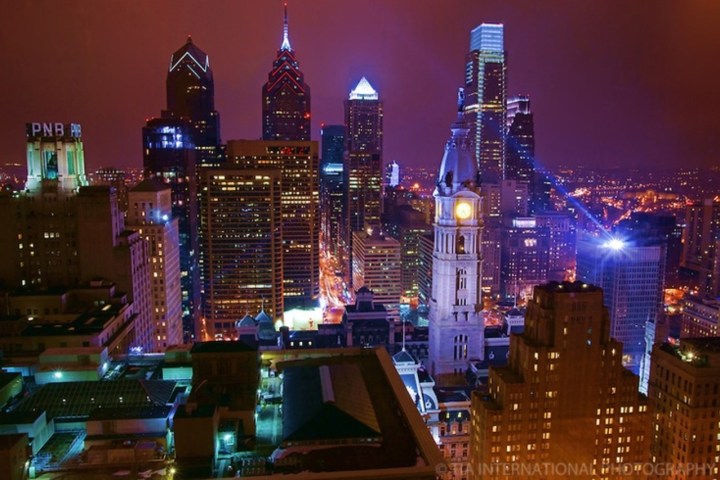 Vibrant city skyline at dusk with brightly lit skyscrapers and a clock tower.