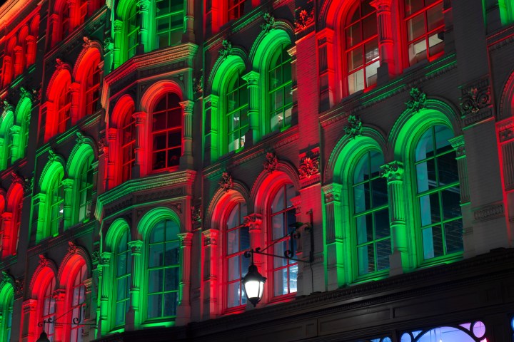 Philadelphia City Hall at night. The large, floor-to-ceiling bay windows are lit up with green and red lights that alternate in a checkered pattern between each set of two bay windows.