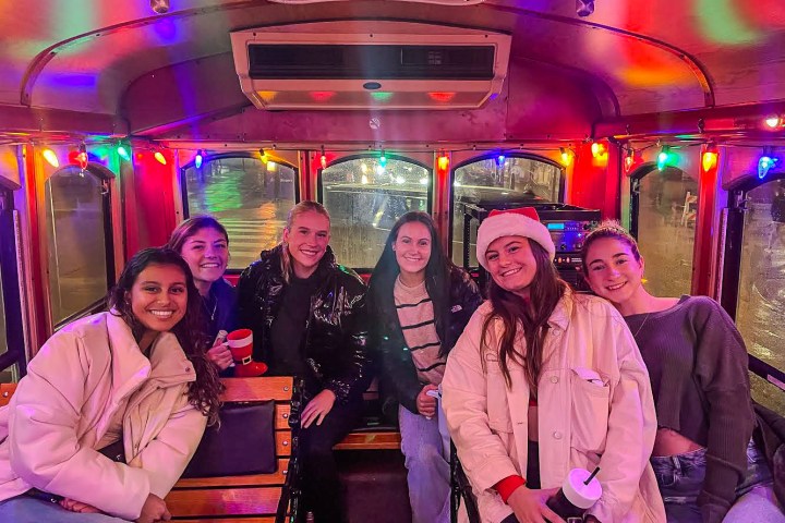 The interior of a City Sightseeing Philadelphia trolley full of happy, smiling people. The ceiling and windows are lined with multicolored Christmas lights that are all lit up in preparation for the Holiday Lights tour.