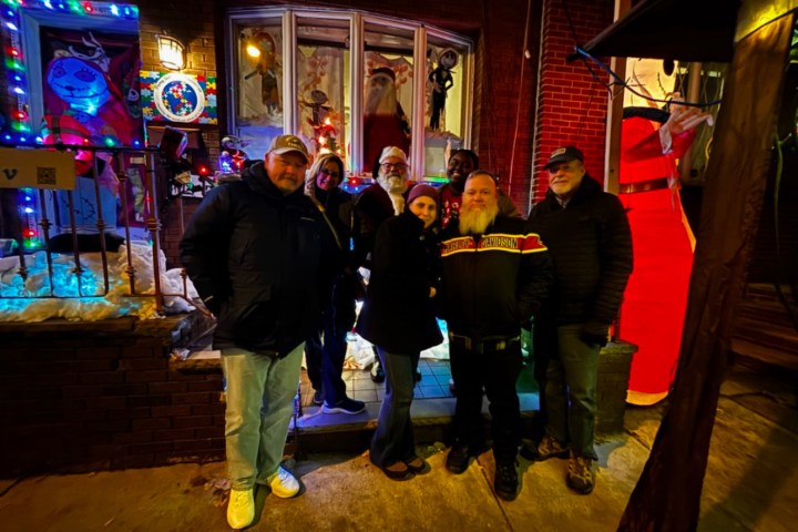 Group of people posing outside a decorated house with colorful lights at night.