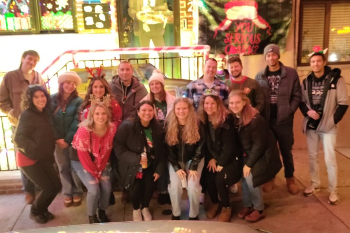 Group of people in festive attire posing on a city sidewalk at night.