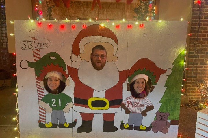 Three people in Santa and elf stand-in cutouts with festive lights and decorations.