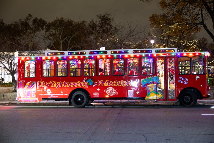Red sightseeing trolley bus with colorful lights in Philadelphia at night.