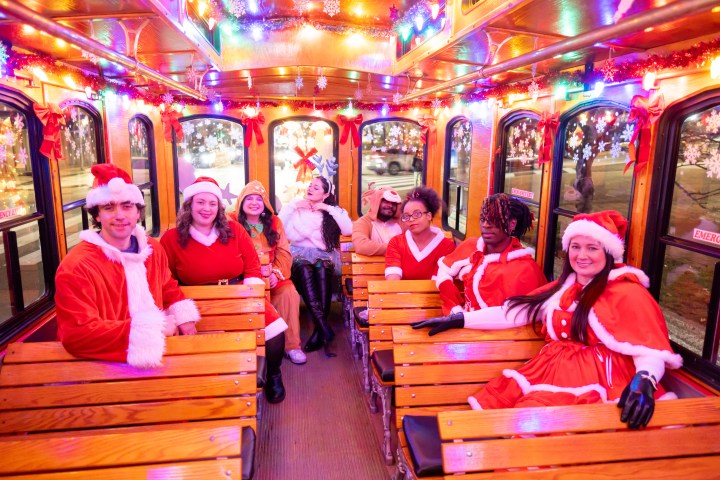 People in festive outfits on a decorated tram with colorful lights and holiday decor.