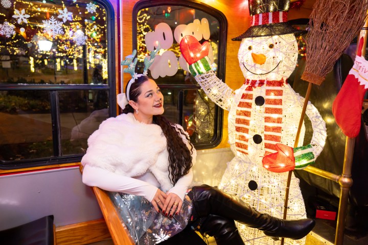 Woman in reindeer antlers sitting with a lit snowman decoration in a festive setting.