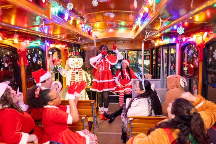 People in festive outfits singing and celebrating inside a decorated trolley.