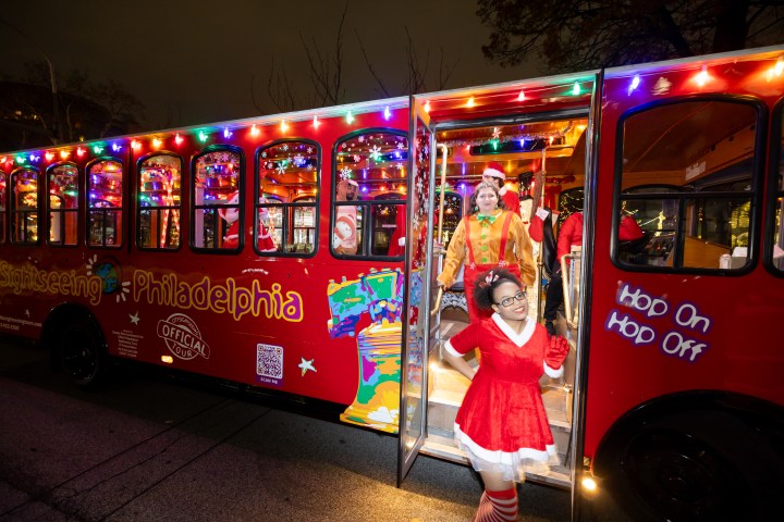 Festive trolley with colorful lights and people in holiday costumes exiting in Philadelphia.