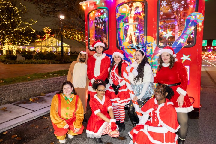 Group in festive costumes near a colorful bus with holiday lights.