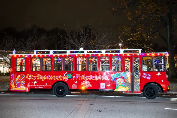 Festively lit red trolley bus for Philadelphia sightseeing, nighttime scene.