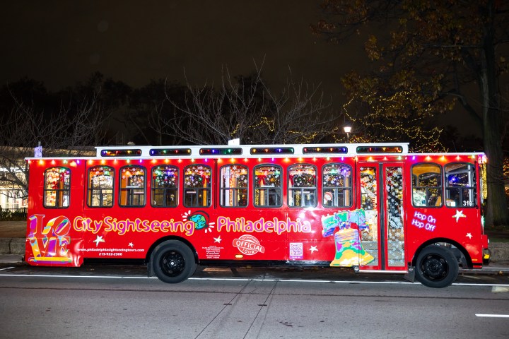 Red sightseeing bus with festive lights parked on a street at night.