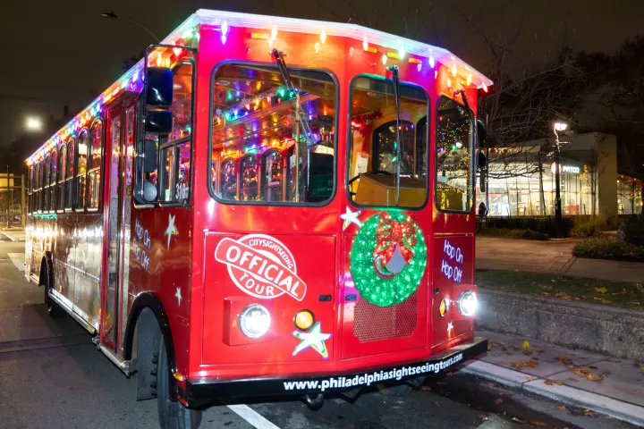 Red trolley bus decorated with colorful lights and a wreath for a city sightseeing tour at night.