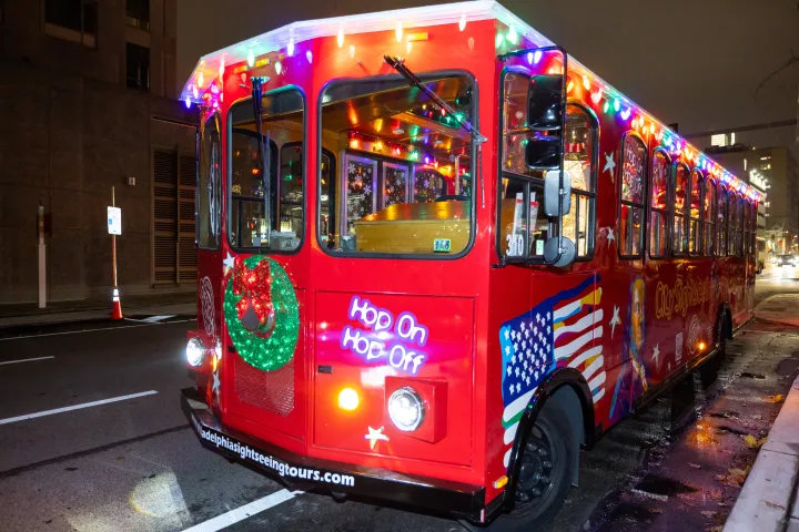 Red trolley bus decorated with lights and a wreath, parked on a street at night.