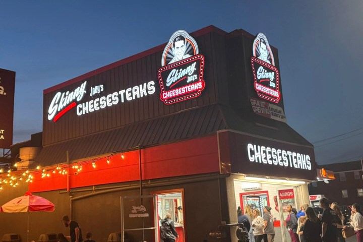 People outside Skinny Joey's Cheesesteaks building at dusk with illuminated signs.