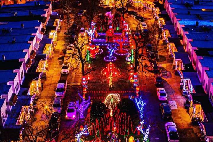 Aerial view of a vibrant residential street decorated with colorful holiday lights at night.